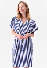 Pasiasta sukienka w niebiesko-białe paski, z dekoltem w kształcie litery V, krótkimi rękawami w stylu nietoperza, wiązanym w pasie oraz luźnym kroju. Gładka tekstura materiału.