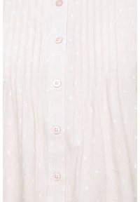 Camicia beige chiaro con pieghe verticali, motivo a pois bianchi e bottoni rosa sul davanti. Realizzata in un tessuto leggero e testurizzato.