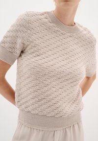 Svetr s krátkým rukávem pletený v jasné béžové barvě s texturovaným diamantovým vzorem. Disponuje žebrovaným kulatým výstřihem a lemem. Měkká tkanina.