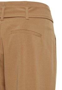 Beige hlače z gladko teksturo, ki vključujejo zadnji žep in paskovne zanke. Tkanina se zdi trpežna in rahlo raztegljiva.