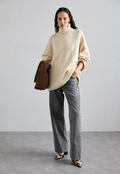 Beige knit turtleneck sweater with loose sleeves, paired with gray wide-leg jeans and animal print heeled shoes. Brown shoulder bag accent.