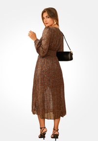 Brązowa midi sukienka w kwiaty z długimi rękawami, ściągnięta w talii i ze zwiewnym dołem. Połączona z czarną torebką i sandałkami na obcasie.