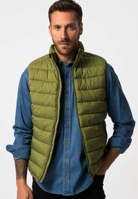 Grön pufferväst med horisontell sömnad över en blå denimskjorta. Vesten har en ståkrage och dragkedja, samt sidofickor.