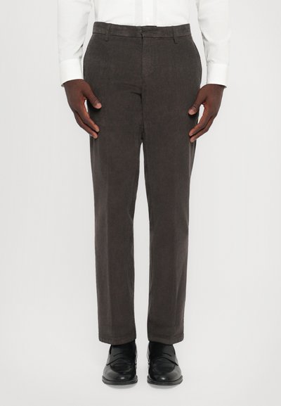 Pantaloni in velluto a coste marroni con vestibilità dritta, caratterizzati da una texture liscia e una parte anteriore piatta. Abbinati a scarpe in pelle nere.