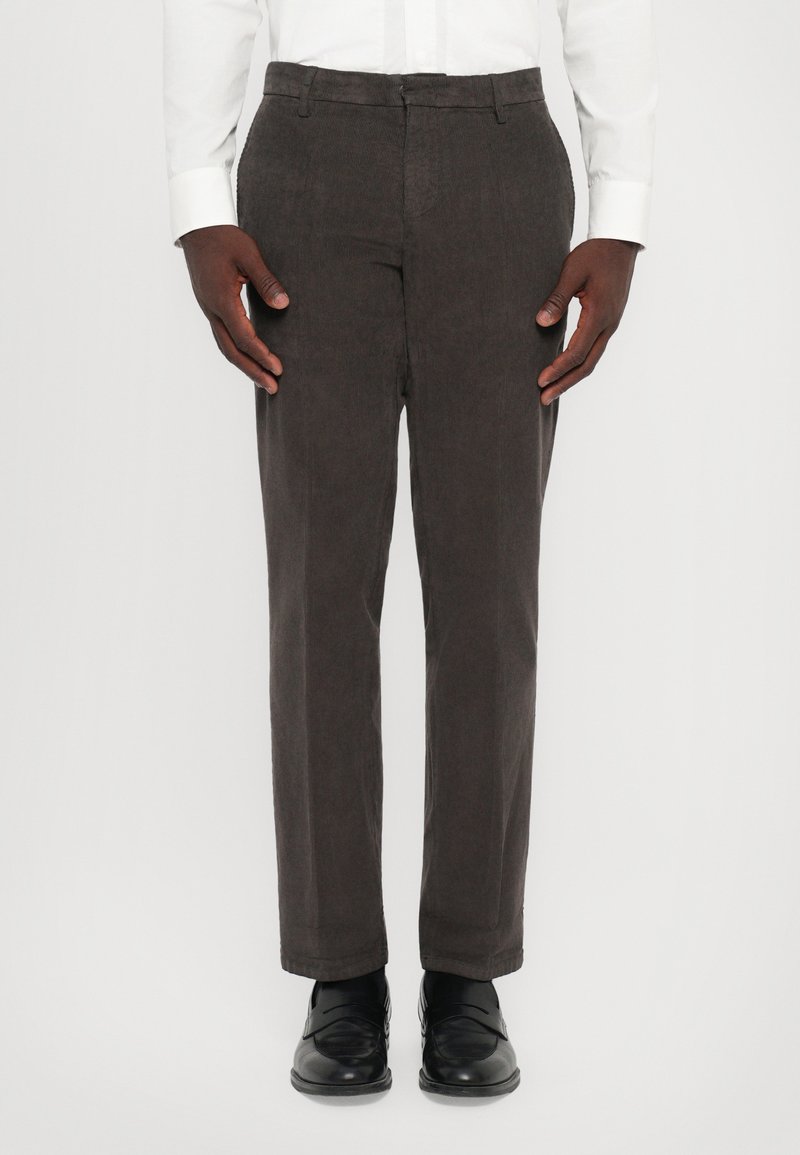 Pantaloni in velluto a coste marroni con vestibilità dritta, caratterizzati da una texture liscia e una parte anteriore piatta. Abbinati a scarpe in pelle nere.