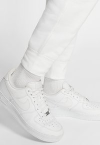 Vita Nike Air Force 1-sneakers med en slät läderöverkant, perforerad tåkappa och vita snören, kombinerade med ribbade vita strumpor och vita joggers.