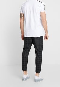 Vit kortärmad t-shirt, svarta byxor med rutmönster och sneakers med genomskinlig sula. Avslappnad passform med kontrasterande axelränder och slim fit-byxor.