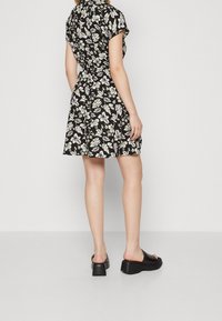 Svart blommig klänning med korta ärmar, markerad midja och utsvängd kjol. Bärs med svarta sandaletter med grov klack. Vitt blommönster över hela.