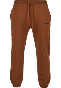 Hnedé bavlnené jogger nohavice s elastickým pásom, sťahovacou šnúrkou, s ukončením na členkoch a malým čiernym logom na ľavom stehne. Hladká textura.