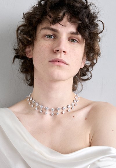 Silberne Halskette mit einem Choker-Design, die mehrere funkelnde klare Edelsteine aufweist und ein wechselndes Muster aus größeren und kleineren Steinen in einer Kettenanordnung zeigt.