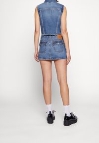 Denimväst med fransad nederkant, i kombination med en matchande denim mini kjol. Har en brun läderpatch, två bakfickor och svarta platåskor.