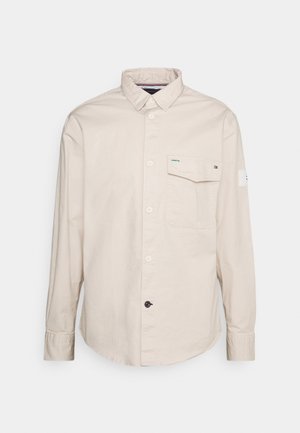 Helles beige Langarmhemd aus Baumwolle mit geknöpftem Frontverschluss, Kragen und einer einzelnen Brusttasche mit Logo-Akzent.