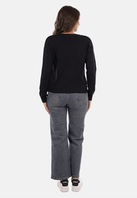 Maglione nero a maglia con maniche lunghe e orlo a costine, abbinato a jeans grigi a vita alta e sneakers nere con dettagli bianchi.