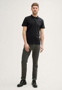 Sort kortærmet polo shirt med krave, parret med grå strukturerede bukser. Footwear inkluderer sorte snøre sko. Enkel design.