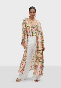 Kimono leggero multicolore con motivi floreali, sovrapposto a un top coordinato e pantaloni bianchi a gamba ampia. Tessuto trasparente, vestibilità ampia.