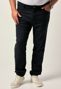 Pantaloni blu scuro realizzati in un tessuto liscio, con un design affusolato e polsini elastici. Indossati con sneaker bianche e una camicia aderente sotto.