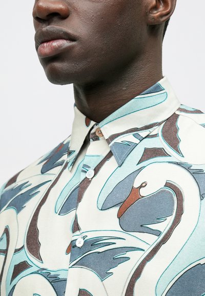 Tričko s krátkym rukávom v svetlo krémovej farbe s motívom labute. Má golier na gombíky, modré a hnedé detaily a hladkú textúru.