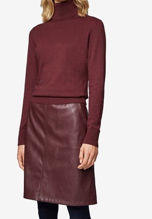 Kvinde i en burgunderfarvet rullekravetrøje kombineret med en matchende burgunderfarvet lædernederdel og sorte leggings.