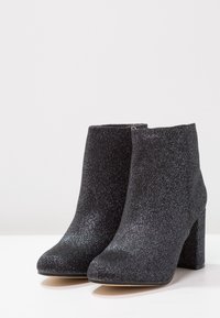 Svarta glittriga ankelstövlar med hög klack, dragkedja på sidan och en slät yta. Passar för formella tillfällen eller kvällsevenemang.