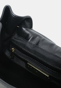 Interno di una borsa a tracolla in pelle nera con una tasca con cerniera. Rivestimento texturizzato e bordi lisci. Dettagli in metallo dorato visibili.