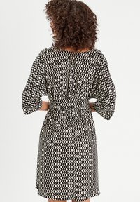 Robe à motif vague noir et blanc avec des manches trois-quarts, taille cintrée et boutons dans le dos. Tissu doux et texturé.