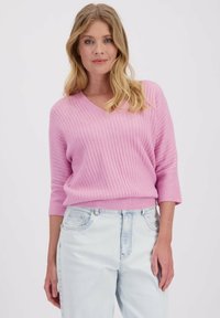Pull en maille côtelée rose clair avec un col en V, des manches 3/4 et une coupe décontractée, associé à un jean bleu clair. Texture somptueuse et tissu doux.