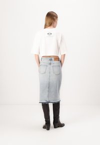 Hvit kortermet T-skjorte med logo på baksiden, parret med en lyseblå denimskjørt og svarte høye støvler, med frynset kant og lommer.