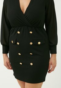 Schwarzes Kleid mit langen, transparenten Ärmeln, einem tiefen V-Ausschnitt und einer taillierten Taille. Verfügt über goldene Knöpfe und zwei Taschen an der Vorderseite.