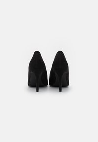 Fekete velúr magassarkú női cipők, hegyes orral és karcsú stiletto sarkakkal, sima felülettel és minimalista dizájnnal.