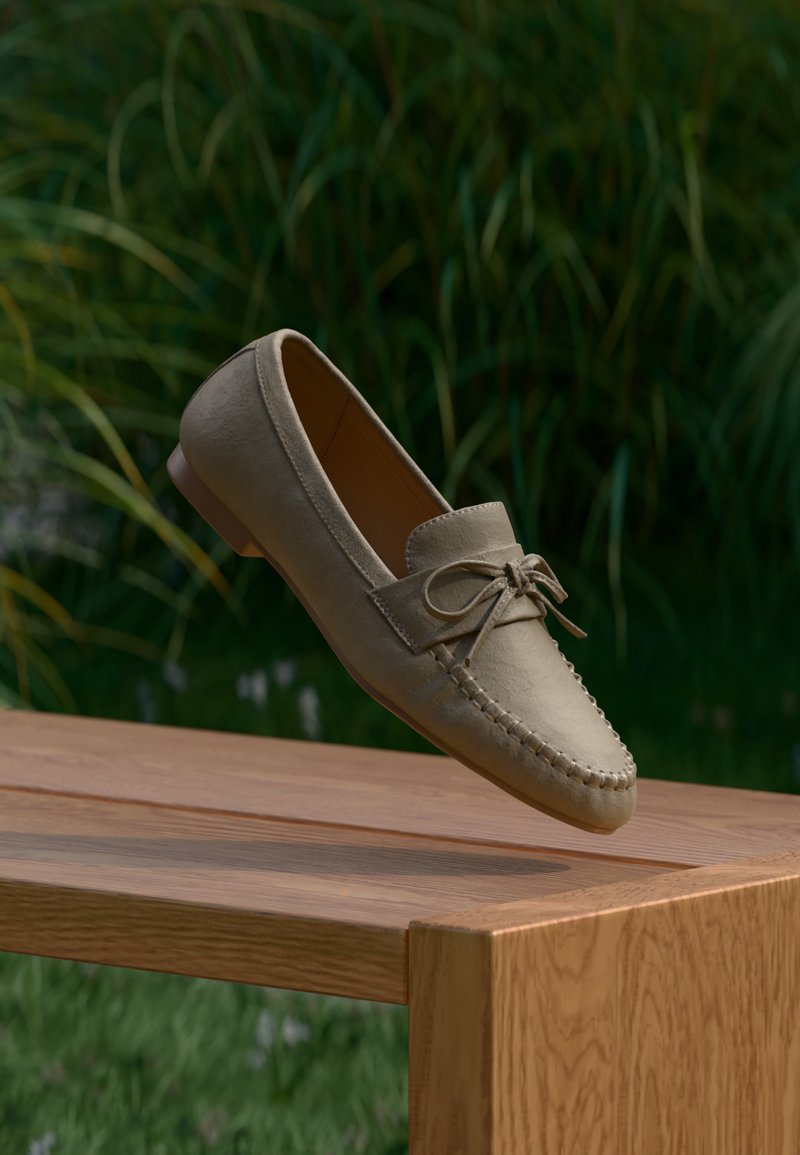 Μπεζ μοκασίνι με φιόγκο που αιωρείται πάνω από ένα ξύλινο παγκάκι, με φόντο πράσινη θολή βλάστηση.