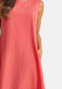 Robe sans manches de couleur pêche avec un col rond et des poches latérales, fabriquée en tissu léger et texturé.