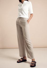 Vit kortärmad polo med krage, beige vida byxor och svarta sandaler med dekorativ hårdvara. Släta texturer genom hela outfiten.