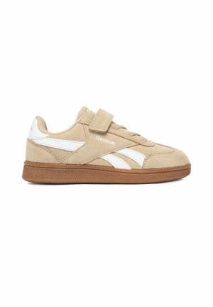 Beżowe zamszowe sneakersy Reebok z białymi paskami, brązową podeszwą i rzepem na beżowych sznurowadłach, widziane z boku.