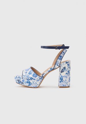 Platform sandaal met hoge hak en blokhak, blauw-wit bloemen- en vlinderpatroon, marineblauwe enkelriem met gesp.