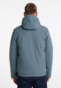 Herrenjacke in gedämpftem Petrol, aus glattem, wasserabweisendem Material. Verfügt über eine Kapuze und elastische Bündchen, mit geradem Schnitt.