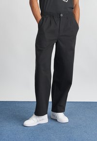 Svart bomullsbukser med avslappet passform, med elastisk midje, sidelommer og en glatt overflate. Brukt med hvite joggesko.