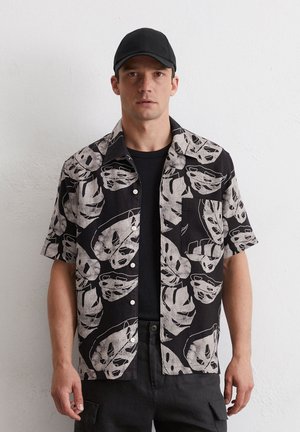 Short-sleeve shirt featuring a black background with large white leaf prints. Includes a front pocket and buttons down the front.