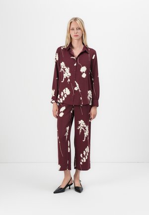 Burgunderfarget skjorte og bukser med blomsterdesign i lett stoff; lange ermer, krage og cropped vide ben; paret med svarte høyhælte sko.