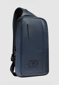 Donkerblauwe leren rugzak met een slank ontwerp, een voorvak met rits en een verstelbare band, voorzien van een subtiel gegraveerd logo en een gestructureerde afwerking.