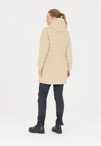 Beige pufferjakke med hætte, med horisontale quiltede linjer. Sammen med sorte bukser og kraftige sorte støvler. Glat tekstur.