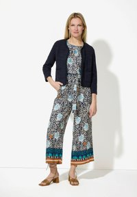 Marinefarbener Langarm-Cardigan über einem blumigen Jumpsuit mit blauen und orangefarbenen Mustern, weit geschnittenen, verkürzten Beinen und beigen Sandalen mit Riemen.