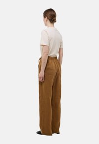 Chemise beige à manches courtes associée à un pantalon en lin marron, ample, avec une taille élastique et deux poches au dos.