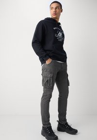 Black hooded sweatshirt with white graphic, paired with dark gray cargo pants featuring side pockets, and black rugged sneakers.