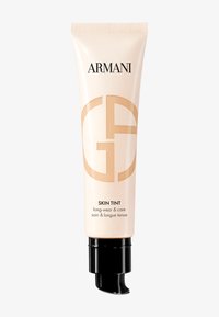 Lys beige tube med en blank finish; har en svart dyse og fremtredende gullbranding; merket "Skin Tint" med produktdetaljer nedenfor.
