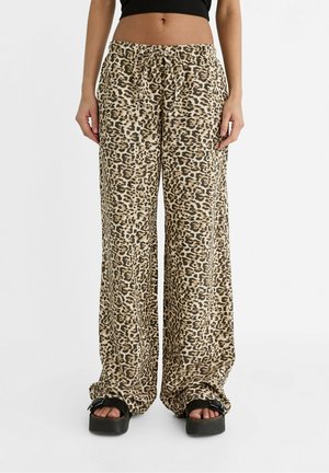 Person wearing beige and black leopard print wide-leg pants with a drawstring waist and black platform slide sandals.