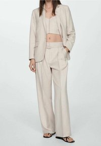 Costume beige sur mesure comprenant un haut court et un pantalon à jambes larges, fabriqu é dans un tissu texturé avec un motif subtil et une taille ceinturée.