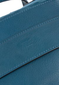 Gros plan d’un cuir bleu avec coutures cousues et texte embossé subtil indiquant "TEMILE Italy."