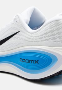 Valge spordijalats, millel on tekstureeritud ülemine osa, must logo ja eristuv sinine vahekiht, millel on markeering "ZOOMX". Omab pehmet krae ja ümarat kuju.