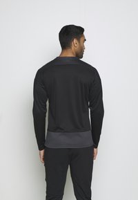 Czarna koszulka sportowa z długim rękawem i szarym dolnym brzegiem. Posiada gładki materiał, klasyczny kołnierzyk oraz dopasowane rękawy.