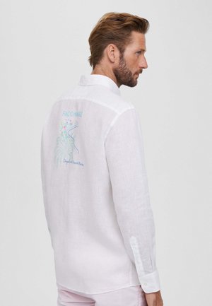 Camisa de lino blanca con un diseño de bordado en la parte posterior que presenta acentos coloridos y el texto "FAÇONNABLE". Mangas largas con puños abotonados.